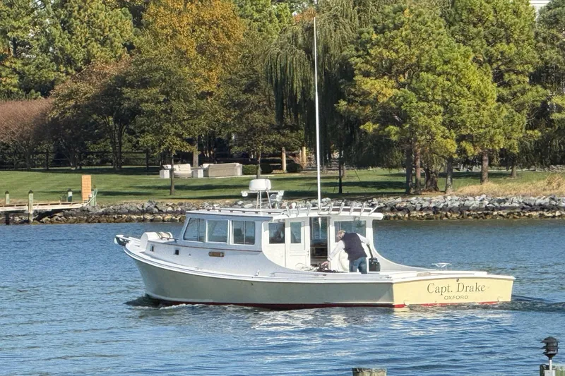 Slide: The Image of Custom 1980 Chesapeake boat "Capt. Drake" on water near lush green shoreline. - 1