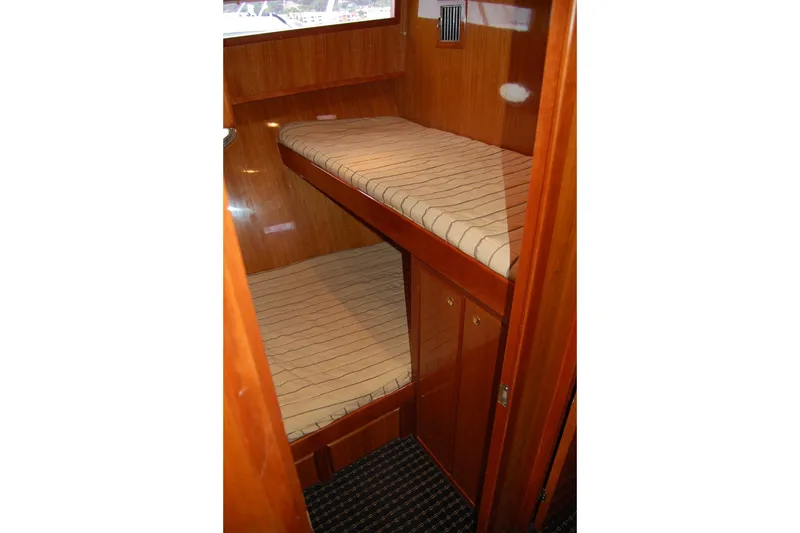 Slide: The Image of 2003 Mikelson Sportfisher cabin with wooden bunk beds and striped mattresses. - 16
