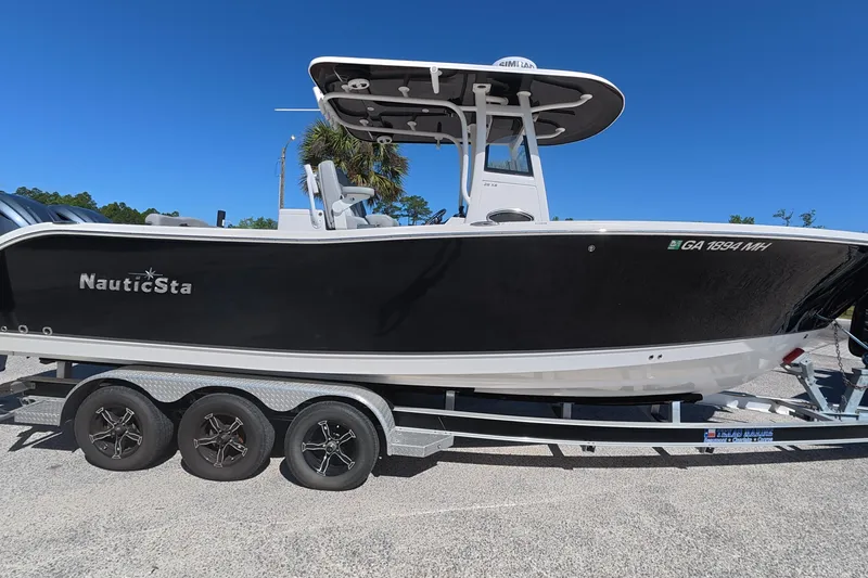 The Image of 2021 NauticStar 28 XS boat on trailer, black hull, clear blue sky background. - 1