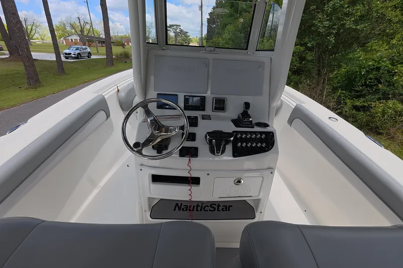 Slide: The Image of 2021 NauticStar 28 XS boat console with steering wheel and controls, surrounded by lush greenery. - 6