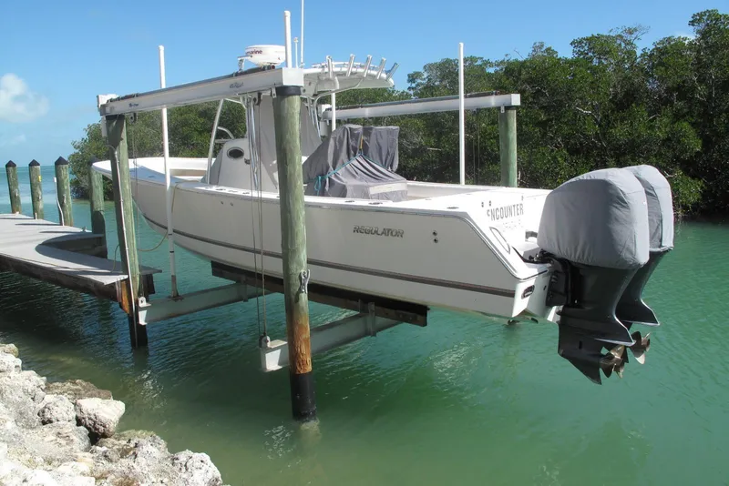Slide: The Image of 2013 Regulator 32 Forward Seating boat on lift by dock, surrounded by water and trees. - 9