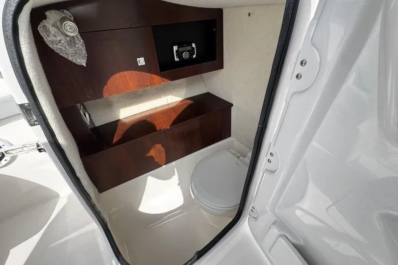 Slide: The Image of 2021 Robalo R227 Dual Console boat interior with compact restroom and wooden cabinetry. - 15