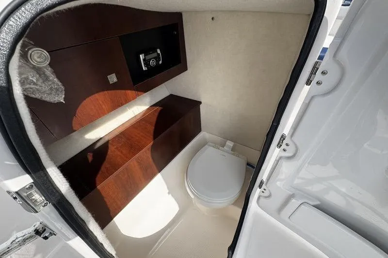 Slide: The Image of 2021 Robalo R227 Dual Console boat interior with compact marine toilet and wooden cabinetry. - 16
