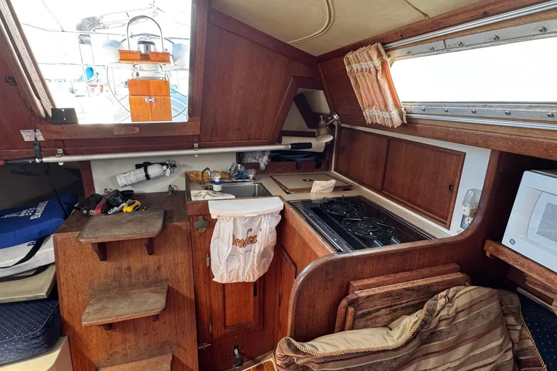 Slide: The Image of 1989 Ericson Sloop interior with wooden cabinetry, compact kitchen, and nautical decor. - 24
