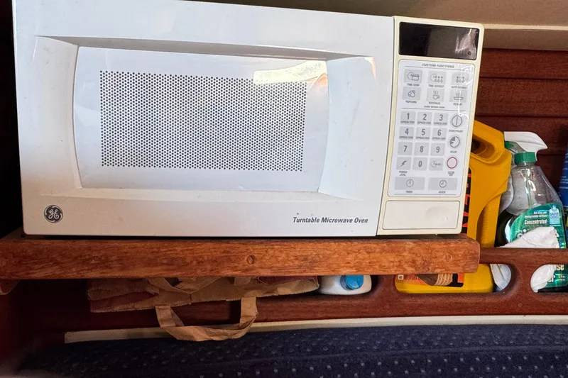 Slide: The Image of Microwave oven inside 1989 Ericson Sloop, surrounded by cleaning supplies and wooden shelving. - 25