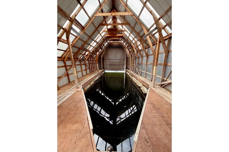 Slide: The Image of Interior of a 1990 BoatHouse 19x43 with wooden beams and reflective water. - 7
