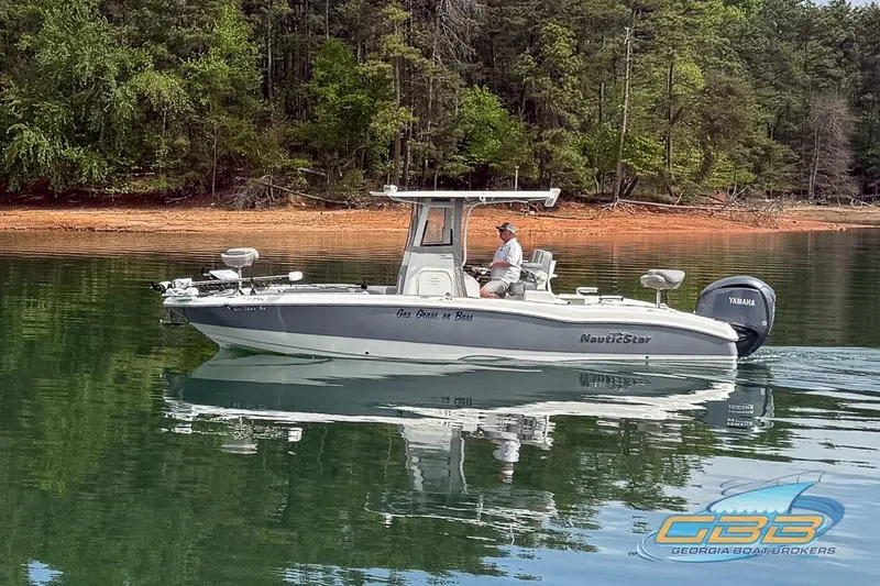 Slide: The Image of 2022 NauticStar 251 Hybrid boat cruising on a calm lake with forested shoreline. - 6