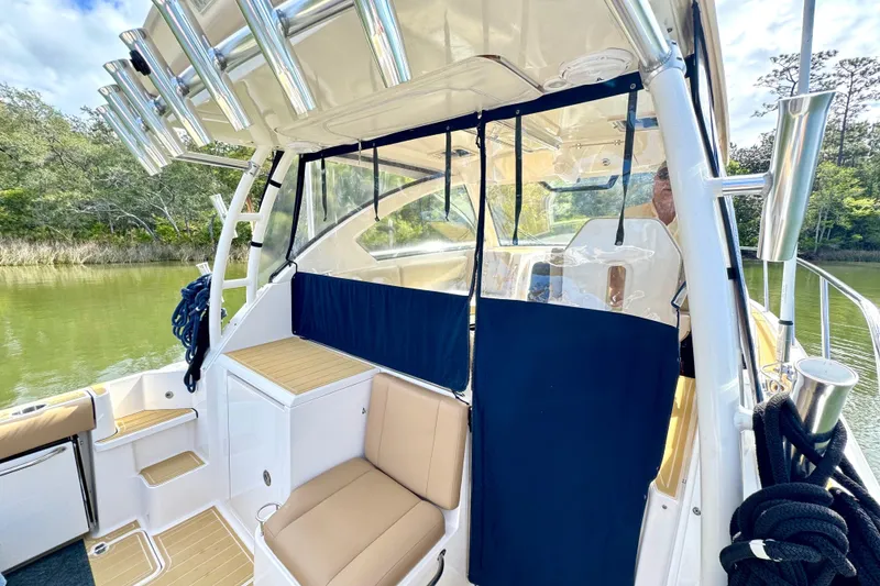 Slide: The Image of 2016 Pursuit OS 325 Offshore boat interior with seating and rod holders, docked by lush greenery. - 14
