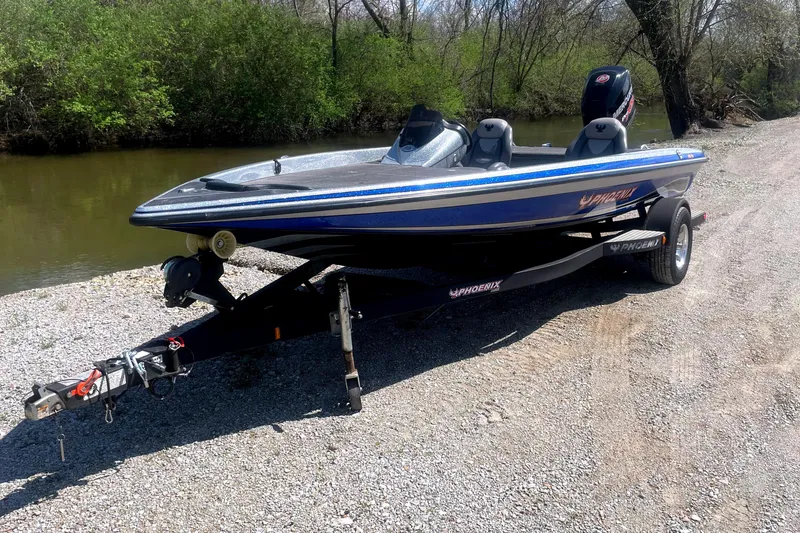 Slide: The Image of 2013 Phoenix 618 Pro boat on trailer by riverside, surrounded by trees. - 2