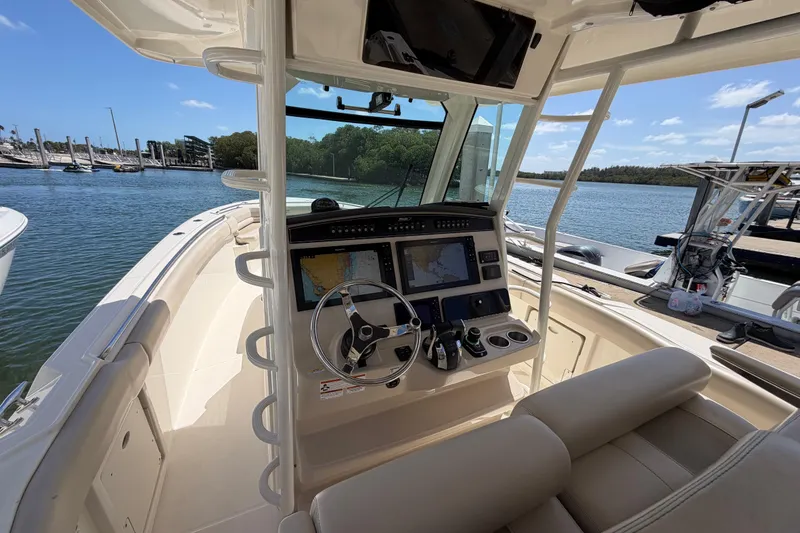 Slide: The Image of 2019 Boston Whaler 330 Outrage helm with navigation screens, docked by a scenic waterfront. - 19