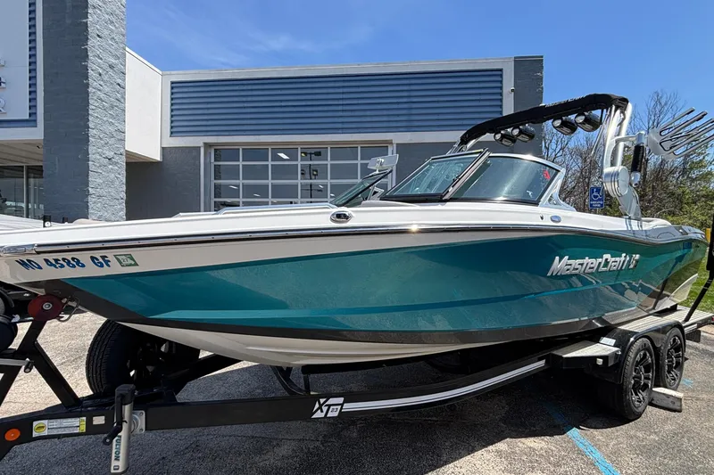 The Image of 2017 MasterCraft XT23 boat on trailer, parked outside a building under a clear blue sky. - 1