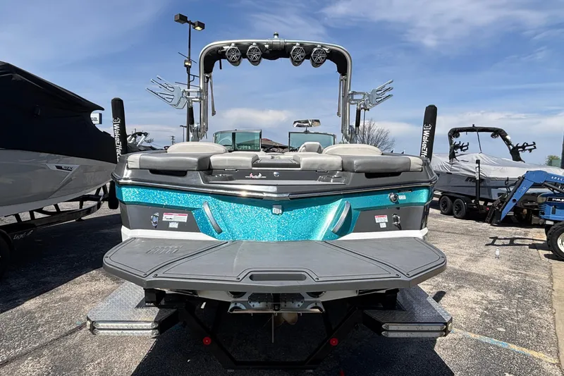 Slide: The Image of 2017 MasterCraft XT23 boat with teal accents, rear view in a marina setting. - 70