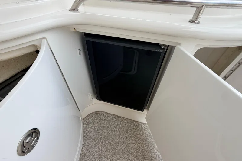 Slide: The Image of 2002 Sea Ray 290 Bowrider interior with open cabinet revealing a compact refrigerator. - 19
