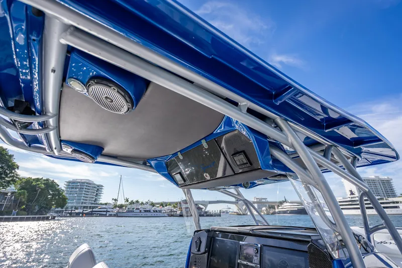 Slide: The Image of 2015 Nor-Tech 340 Sport Center Console boat with blue canopy and speakers, docked by waterfront. - 37