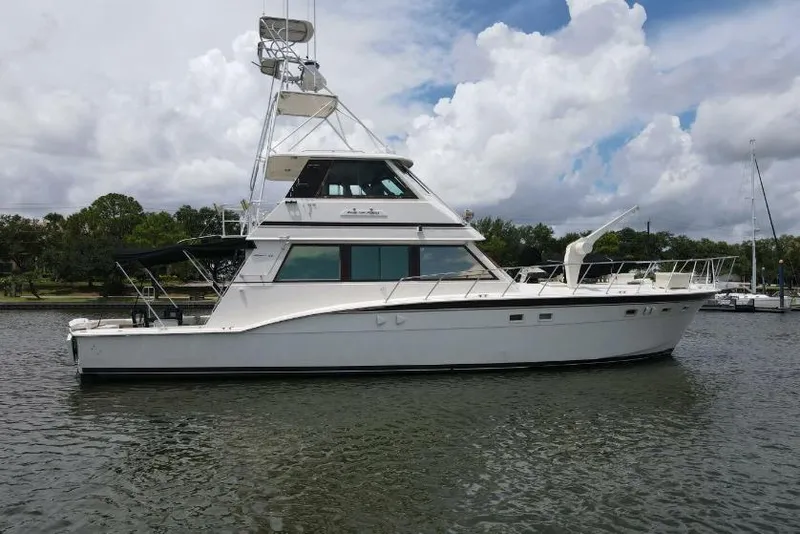 The Image of 1985 Hatteras 60 Convertible yacht on calm water under cloudy sky. - 1