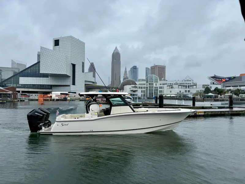 Slide: The Image of A Scout 330 LXF boat navigates through an urban harbor with modern buildings in the background. - 0