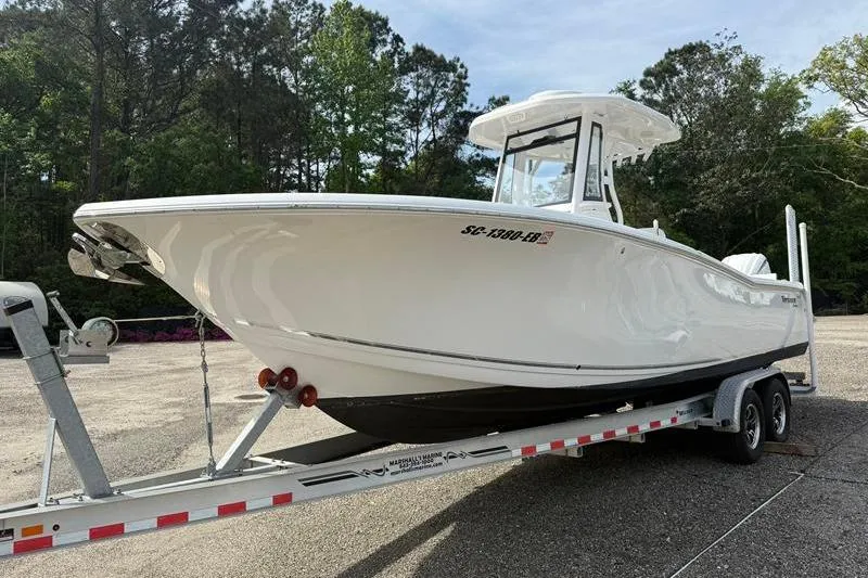 Slide: The Image of 2022 Tidewater 272 LXF boat on trailer, parked outdoors with trees in background. - 6
