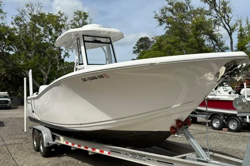 Slide: The Image of 2022 Tidewater 272 LXF boat on trailer, parked outdoors with trees in background. - 8