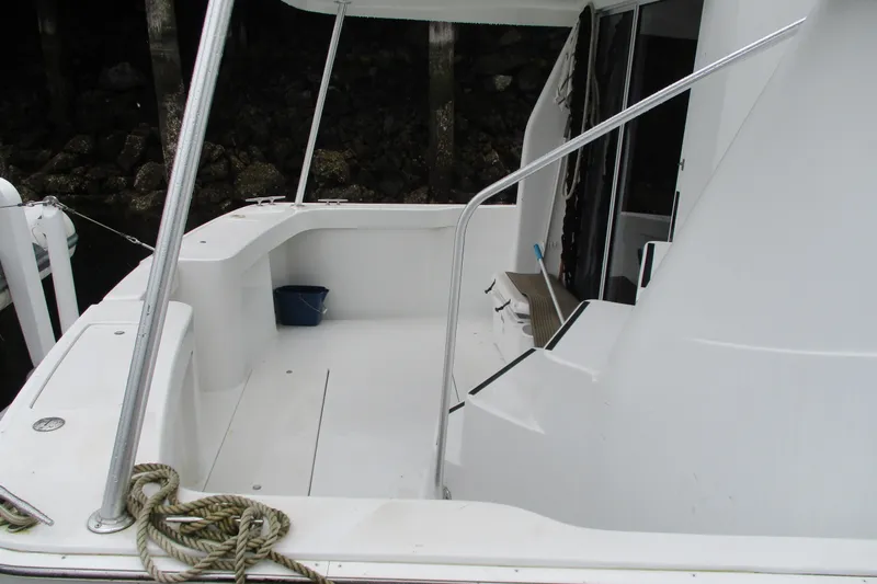 Slide: The Image of 1997 Mainship 350 Trawler deck area with seating and railing, docked near rocky shoreline. - 11