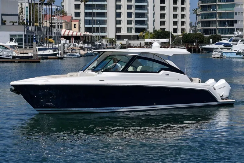 The Image of 2026 Tiara Yachts 34 LX cruising in a marina with modern buildings in the background. - 1
