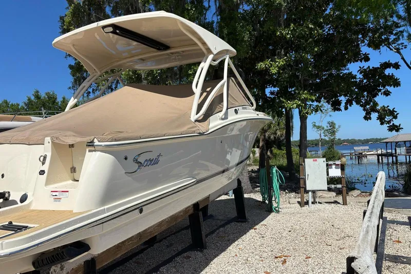 Slide: The Image of 2024 Scout 255 Dorado boat on a stand by a lakeside, under clear blue skies. - 8