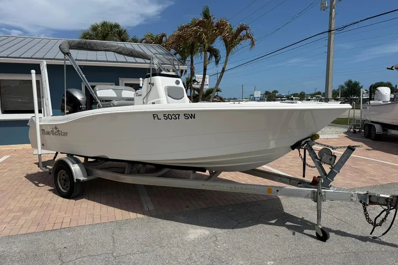 Slide: The Image of 2021 NauticStar 191 Hybrid boat on trailer, parked outdoors near a blue building. - 7