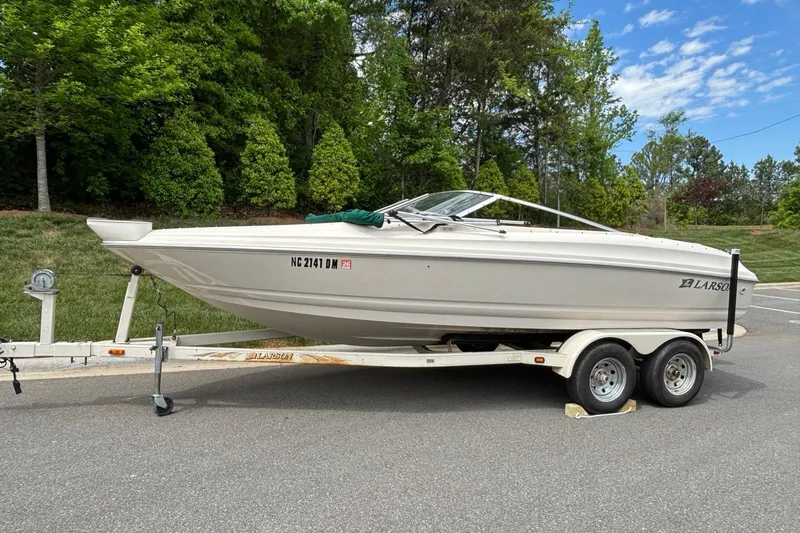 The Image of 2001 Larson 210 I/O boat on trailer, parked on roadside with lush greenery background. - 0