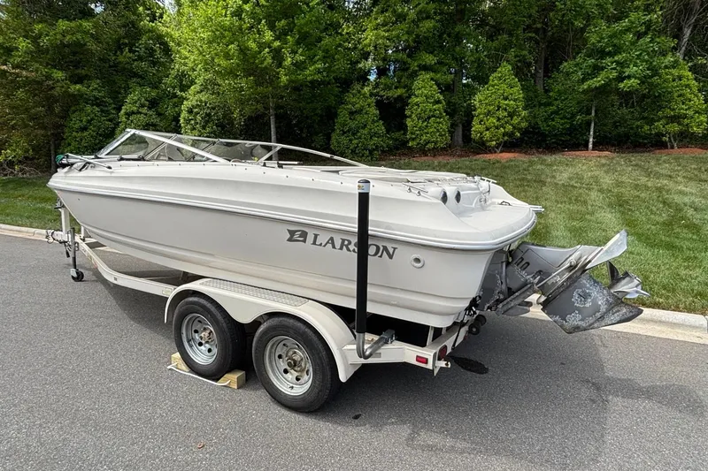 Slide: The Image of 2001 Larson 210 I/O boat on trailer, parked on a paved road with greenery background. - 2