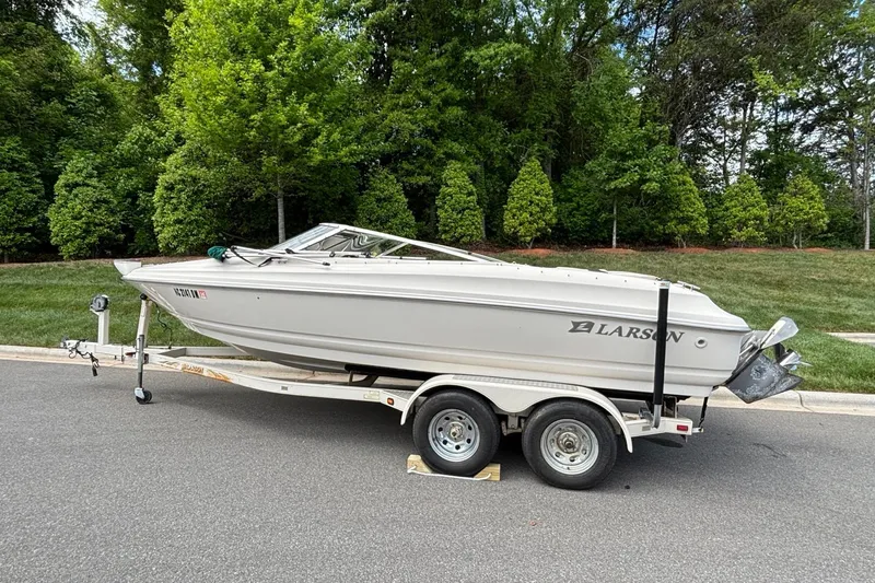 Slide: The Image of 2001 Larson 210 I/O boat on trailer, parked on a road with lush greenery background. - 3