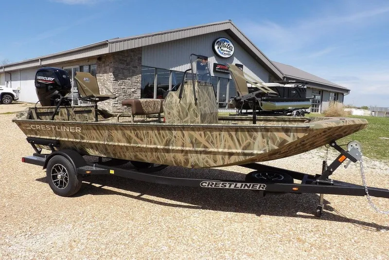 The Image of 2026 Crestliner 1760 Retriever FCC boat with camouflage design on a trailer outside a marine store. - 1