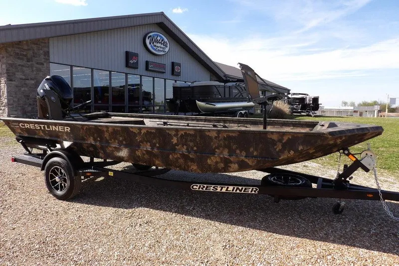 The Image of 2026 Crestliner 1860 Retriever Deluxe boat with camouflage design on a trailer outside a marine center. - 1