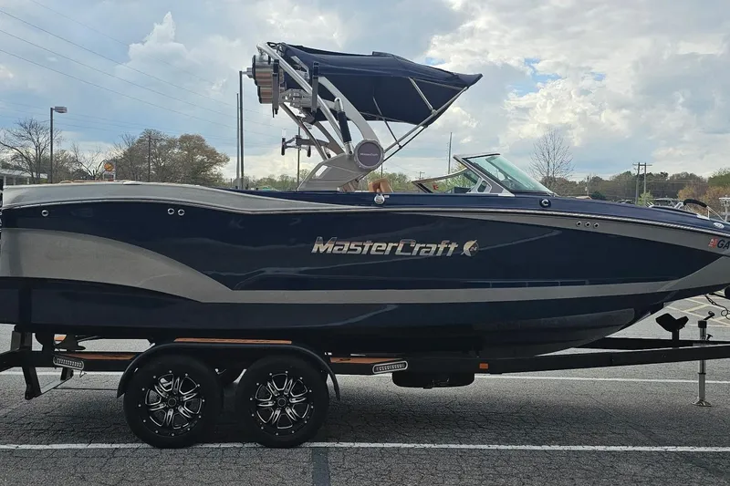 Slide: The Image of 2020 MasterCraft X24 boat on trailer, parked outdoors under cloudy sky. - 19