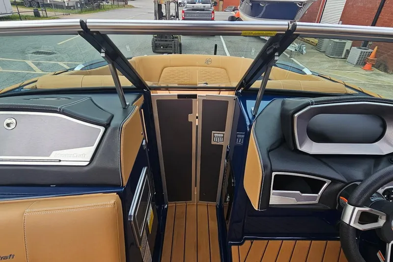 Slide: The Image of 2020 MasterCraft X24 boat interior with tan and black seating, sleek dashboard, and wooden flooring. - 43