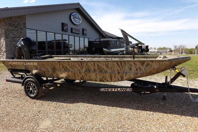 The Image of 2026 Crestliner 1860 Retriever Deluxe boat with camouflage design on a trailer outside a marine center. - 2