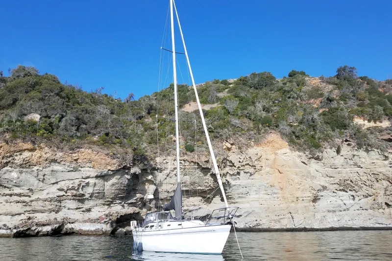 Slide: The Image of Sailboat Islander Peterson 40 (1979) anchored near rocky coastline under clear blue sky. - 2