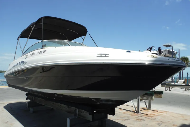 Slide: The Image of 2005 Sea Ray 220 Sundeck boat with black hull and canopy, docked under clear blue sky. - 2