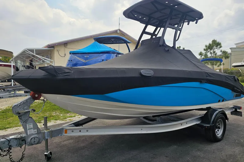Slide: The Image of 2022 Yamaha Boats 190 FSH Sport, blue hull, covered, on trailer, outdoor display. - 9