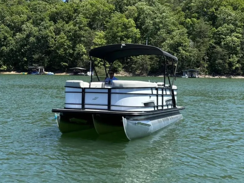 Slide: The Image of A 2025 Starcraft EXS 1 pontoon boat on a calm lake, surrounded by trees. - 1