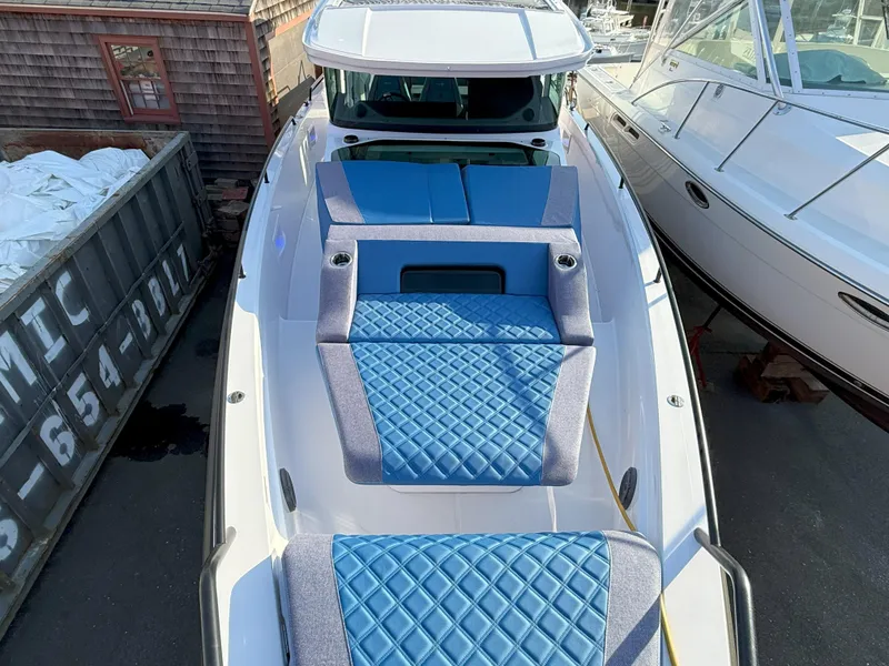 Slide: The Image of 2024 Axopar Cross Cabin boat with blue cushioned deck, docked beside other vessels. - 4