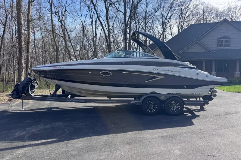 Slide: The Image of 2022 Crownline 265 SS boat on trailer, parked in driveway near wooded area. - 2
