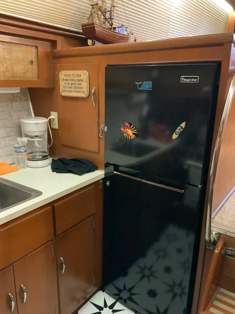 Slide: The Image of 1969 Hatteras 41 Double Cabin kitchen with black fridge, wooden cabinets, and nautical decor. - 41