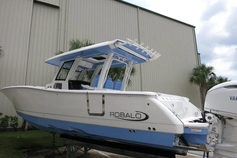 Slide: The Image of 2025 Robalo R360 Center Console boat with blue and white design, docked outdoors. - 26