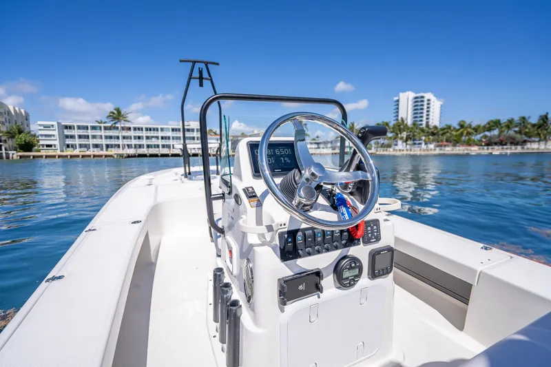 Slide: The Image of 2026 Spyder FX19 Vapor boat steering console on calm waters, with buildings and palm trees in background. - 28