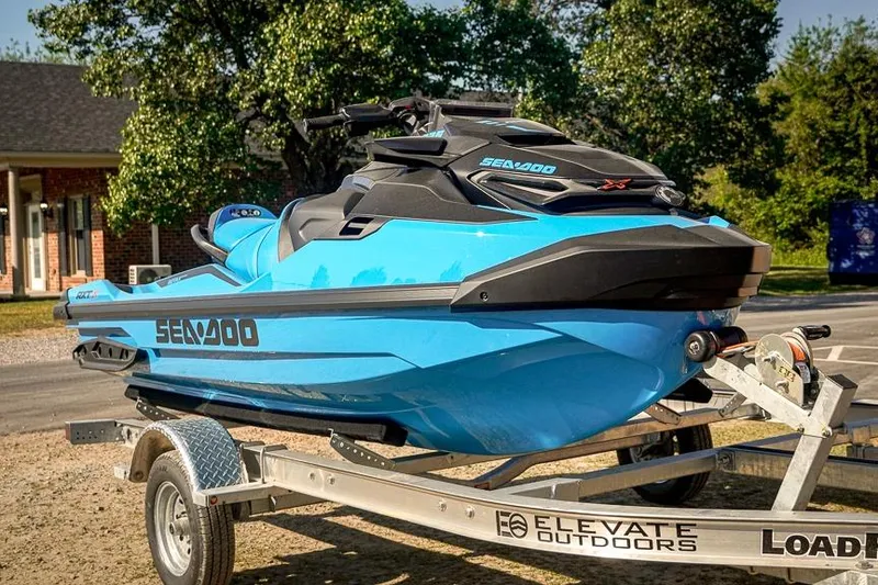 Slide: The Image of 2026 Sea-Doo RXT-X 325 jet ski on trailer, vibrant blue, parked outdoors. - 2