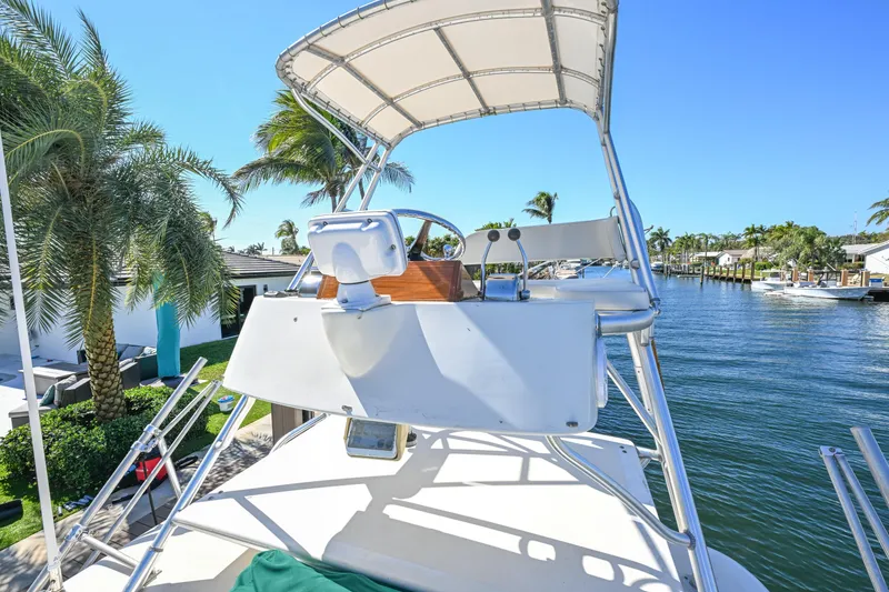 Slide: The Image of 2000 Pursuit 3400 Express boat helm with canopy, docked near palm trees and waterfront homes. - 15