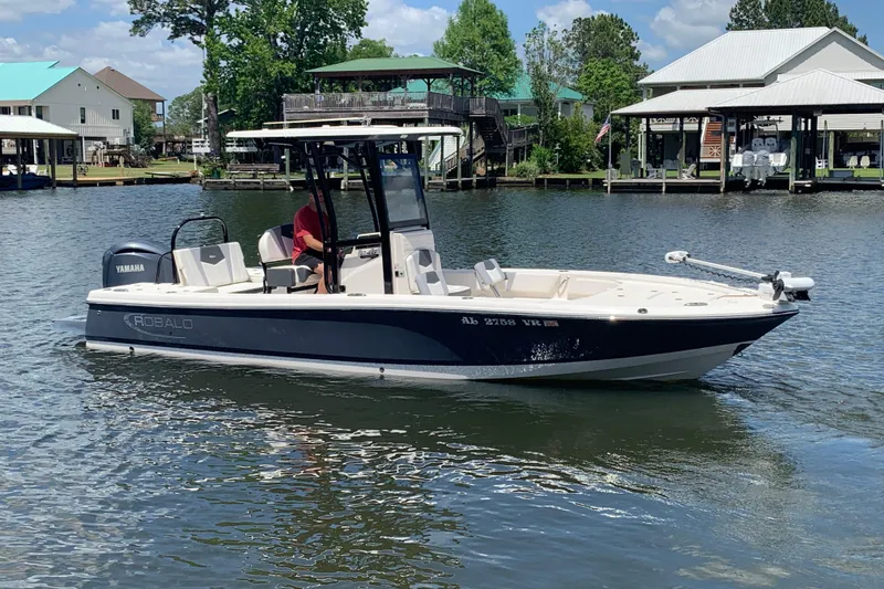 Slide: The Image of 2022 Robalo 246 Cayman boat on a calm lake with waterfront homes in the background. - 2