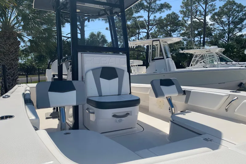 Slide: The Image of 2022 Robalo 246 Cayman boat interior with seating and console, surrounded by trees. - 9