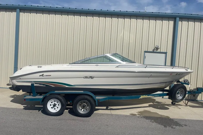 The Image of 1996 Sea Ray 210 Bow Rider boat on trailer, parked by a metal building. - 0