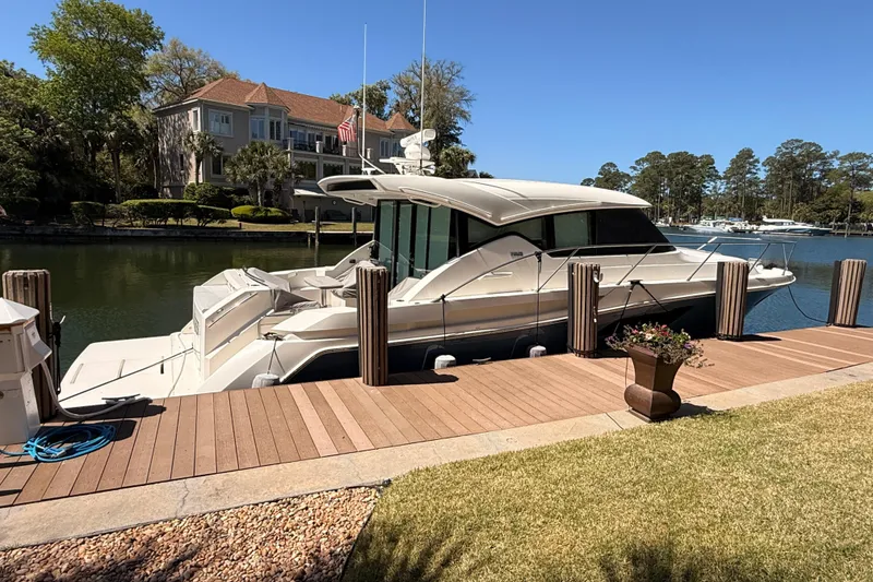 The Image of 2020 Tiara Yachts C44 Coupe docked by a luxurious waterfront home with palm trees. - 0