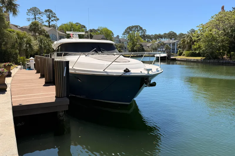 Slide: The Image of 2020 Tiara Yachts C44 Coupe docked by a waterfront home, surrounded by lush greenery. - 2
